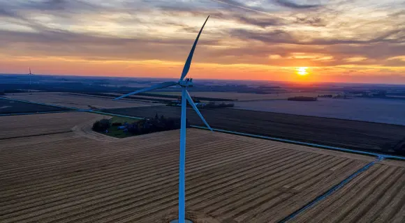 Wind turbine standing in open farmland at sunset