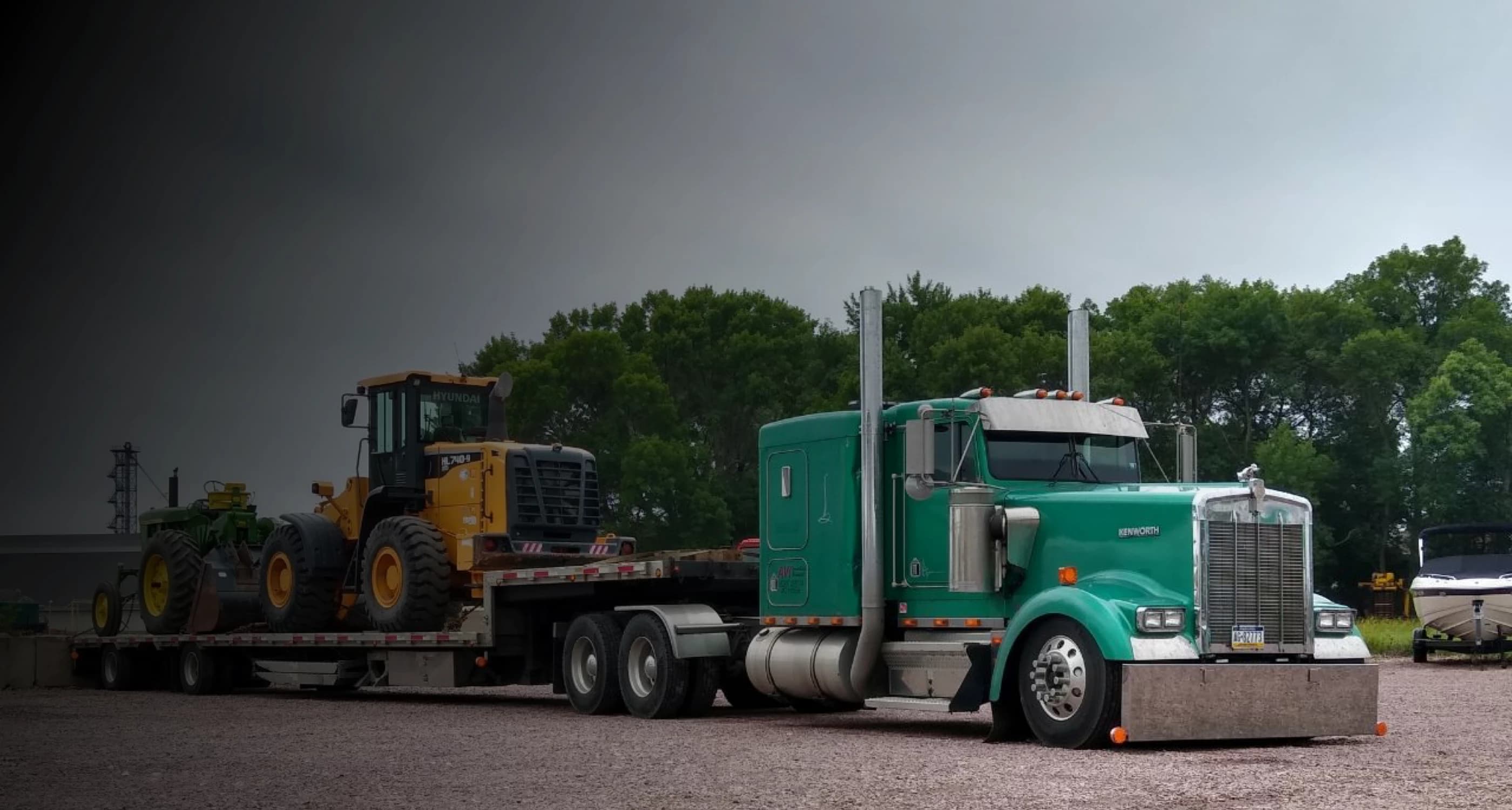 Wheel loader and tractor loaded on a lowboy trailer behind a green heavy-haul truck