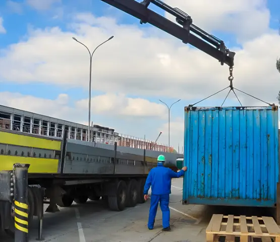 Crane lifting a steel container from a trailer at an industrial yard