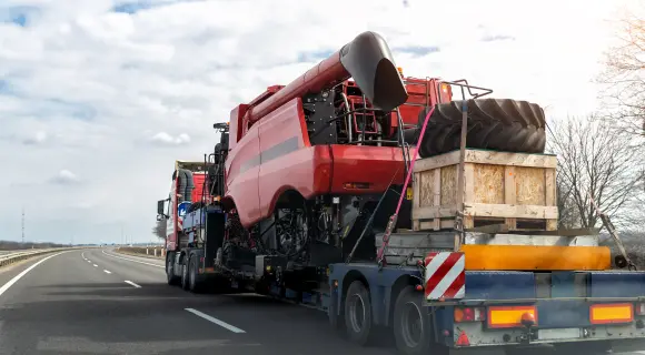 Red combine harvester carried on a lowbed trailer along a multi-lane highway